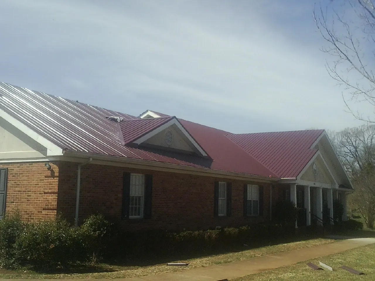 Red metal roof with gabled entries on a long brick building, from a Hail Damage Roof Repair job in Winfield