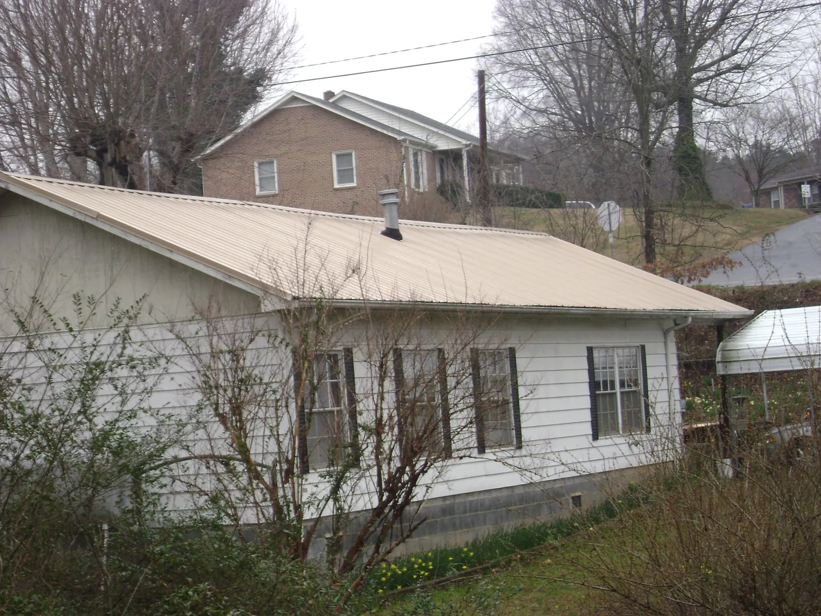 Tan metal roof on a white sided house set into a hillside — Commercial Roofing by Roofing Brothers in Winfield